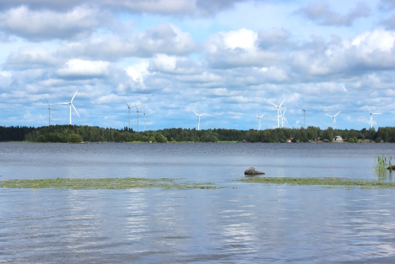 Tuulivoimaloita horisontissa, vesistön ja metsän takana.